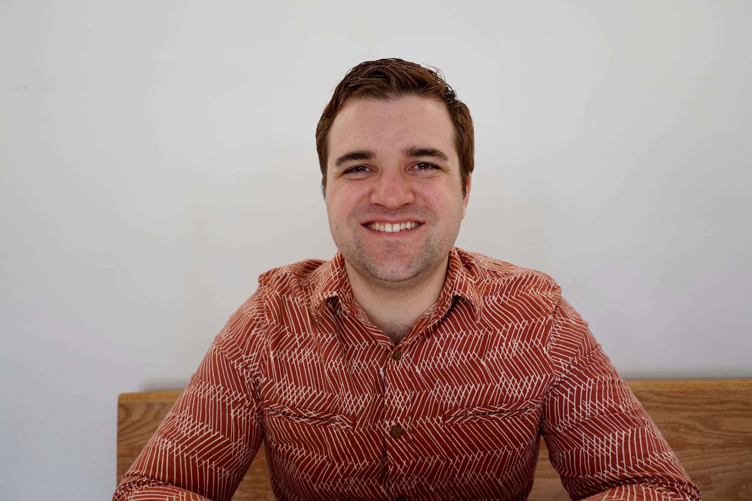 Brett Wharton seated against a white wall, smiling