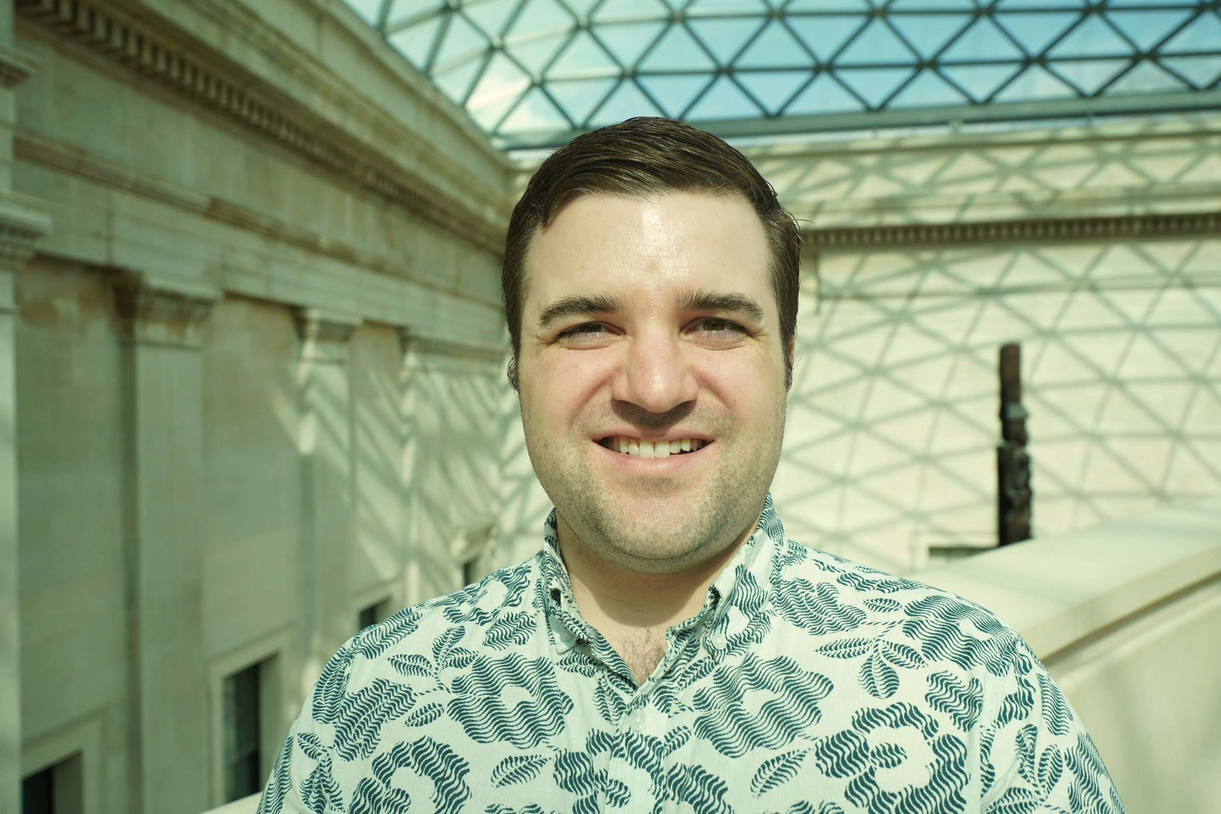 Brett Wharton beneath the glass roof of a museum court, smiling