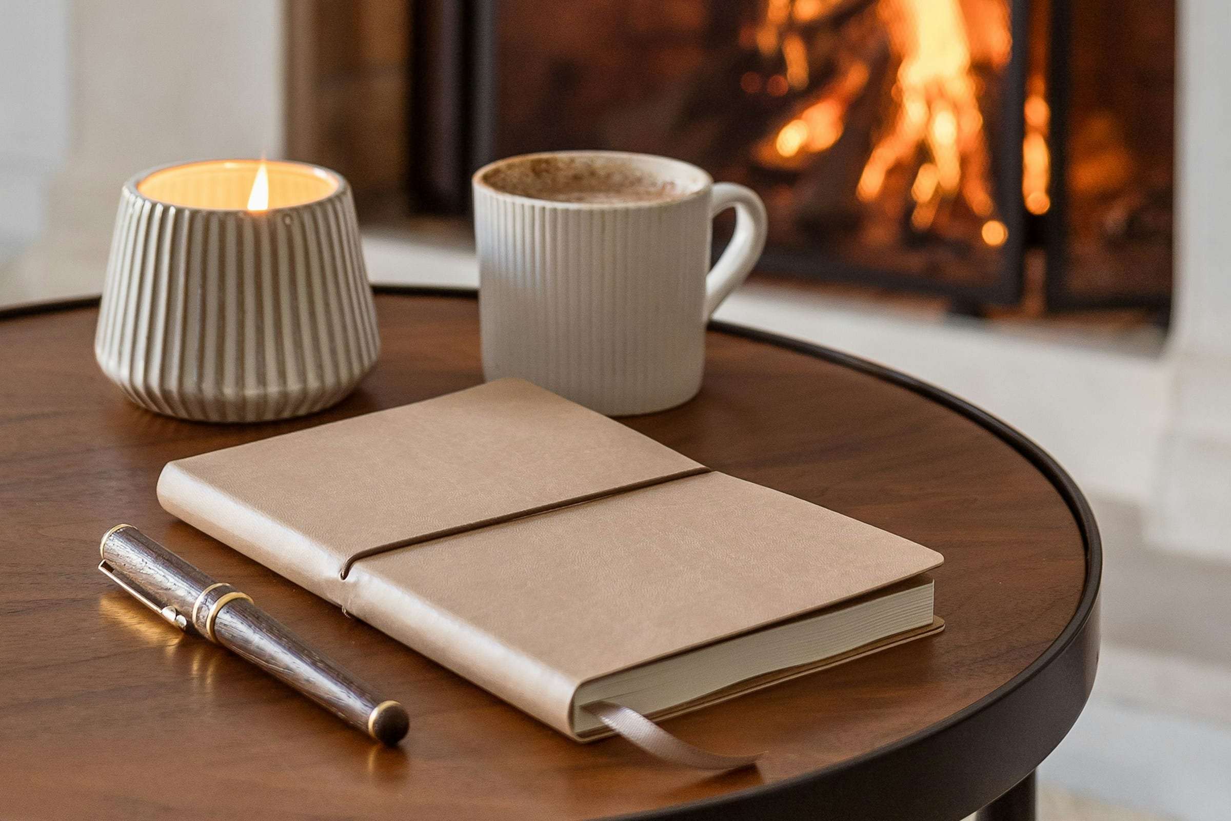 A closed notebook and pen on a table beside a fire
