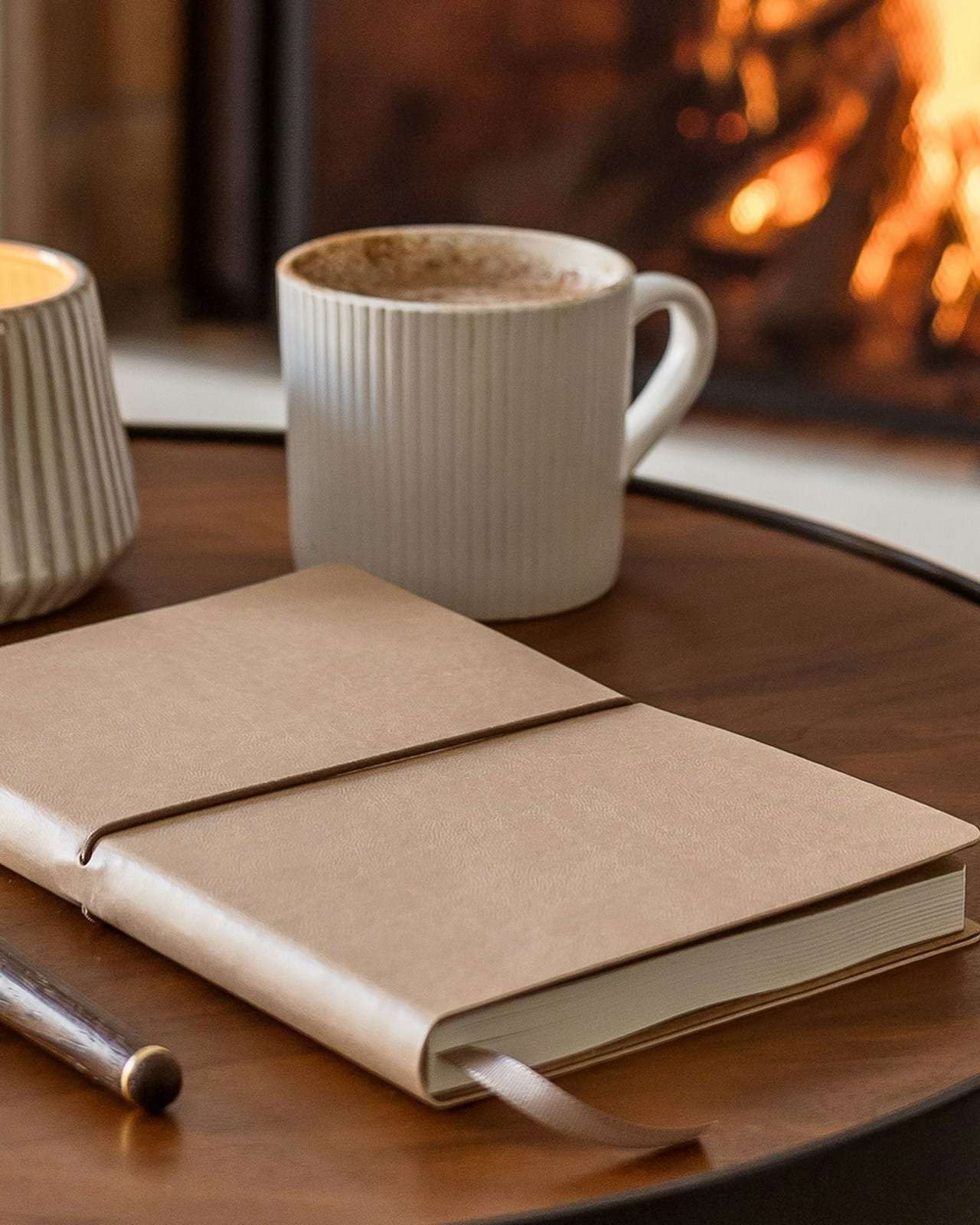 A closed notebook and pen on a table beside a fire