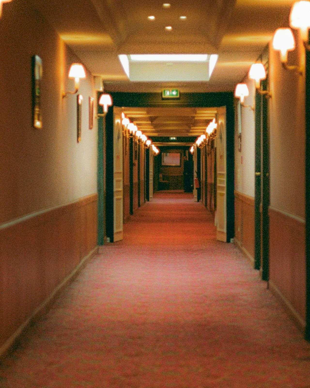 A long hotel corridor with a red carpet and wall sconces, empty