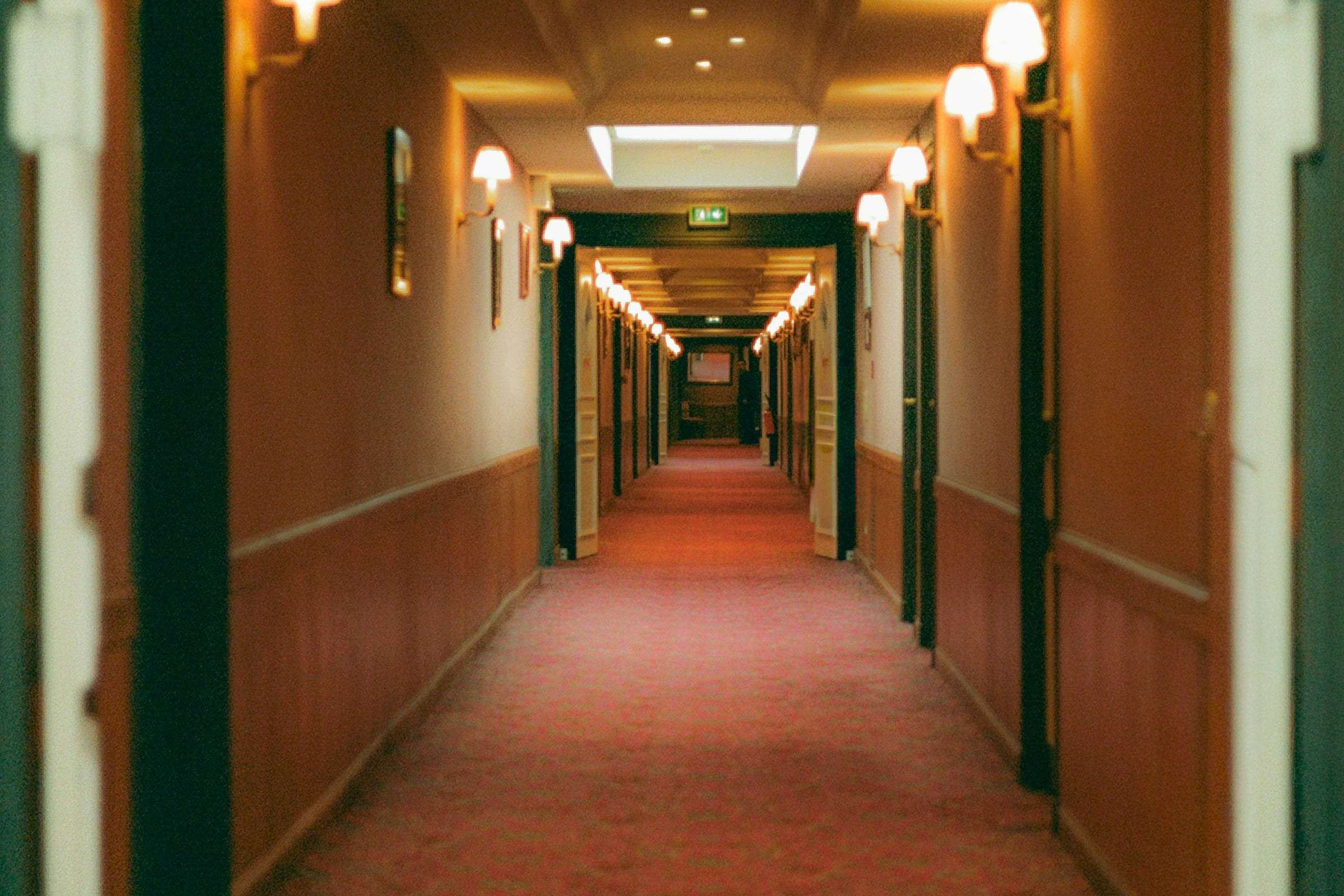 A long hotel corridor with a red carpet and wall sconces, empty