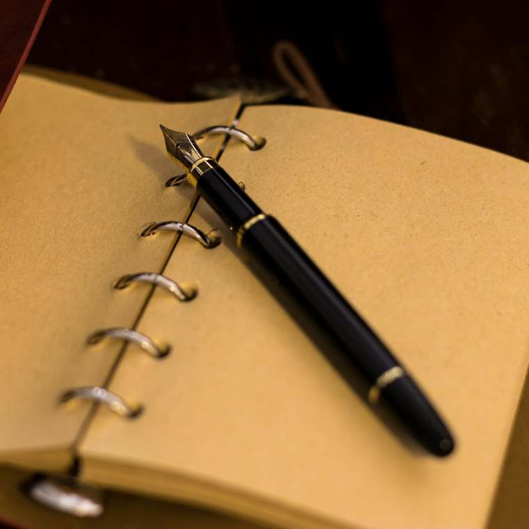 A fountain pen resting on the open pages of a leather notebook