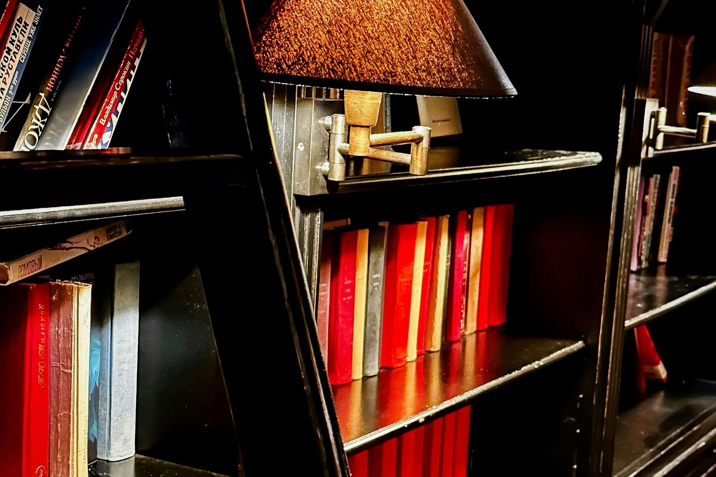 A library ladder against dark shelves with a small lamp