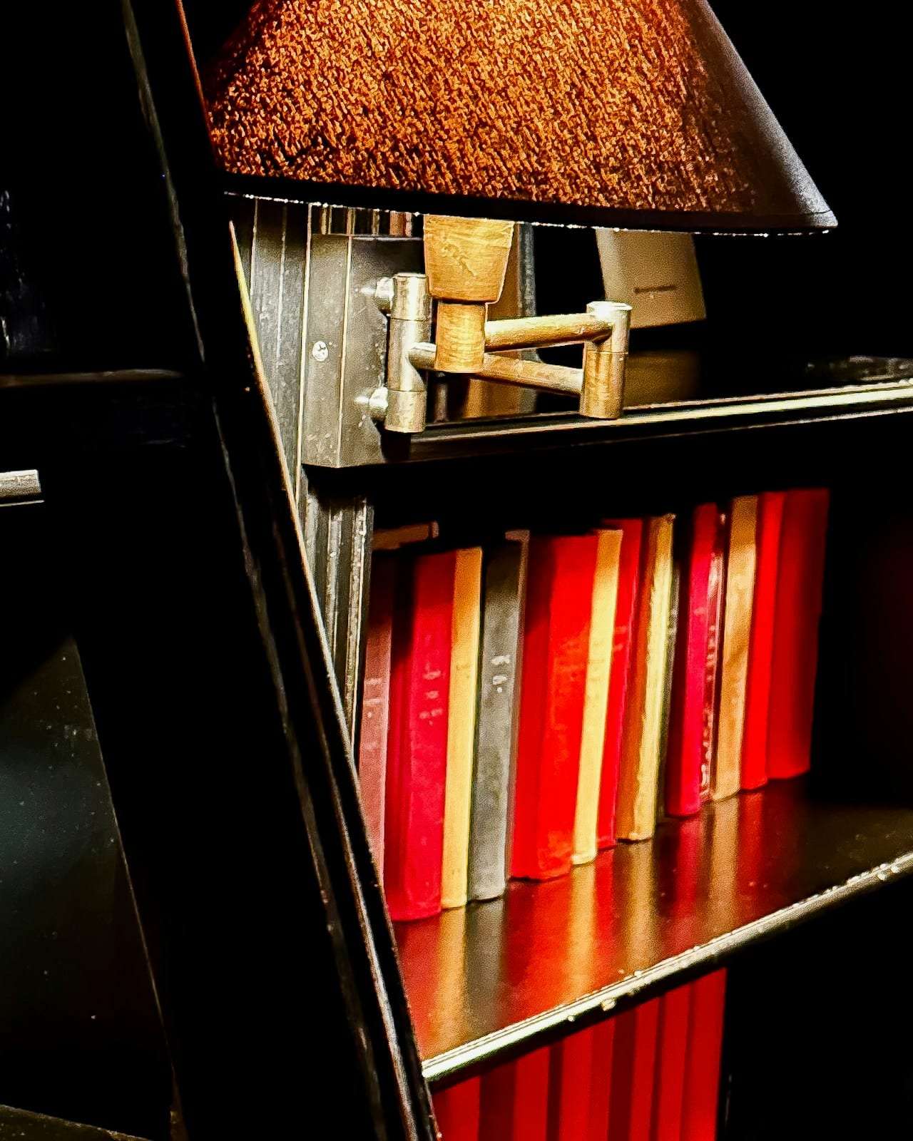 A library ladder against dark shelves with a small lamp