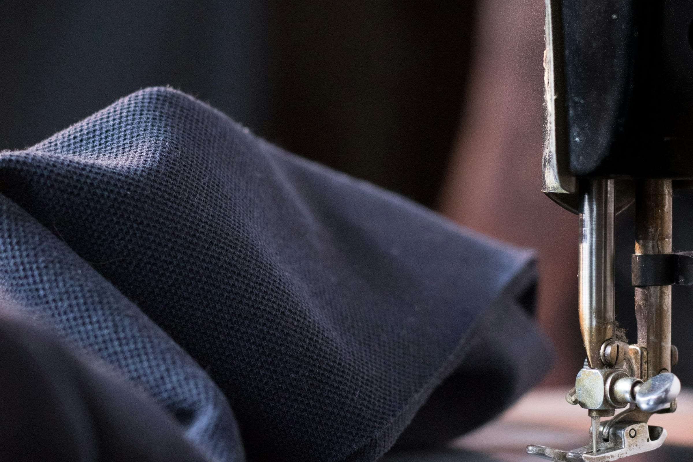 Navy wool cloth beneath the foot of a tailor’s sewing machine